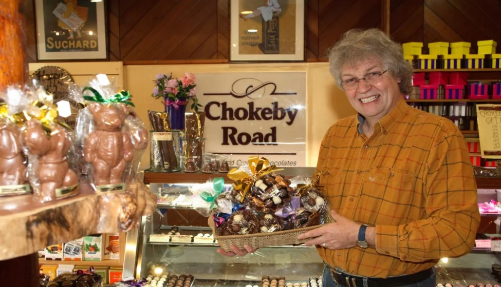 Richard Blance holding a basket of handmade chocolates behind the counter at Chokeby Road