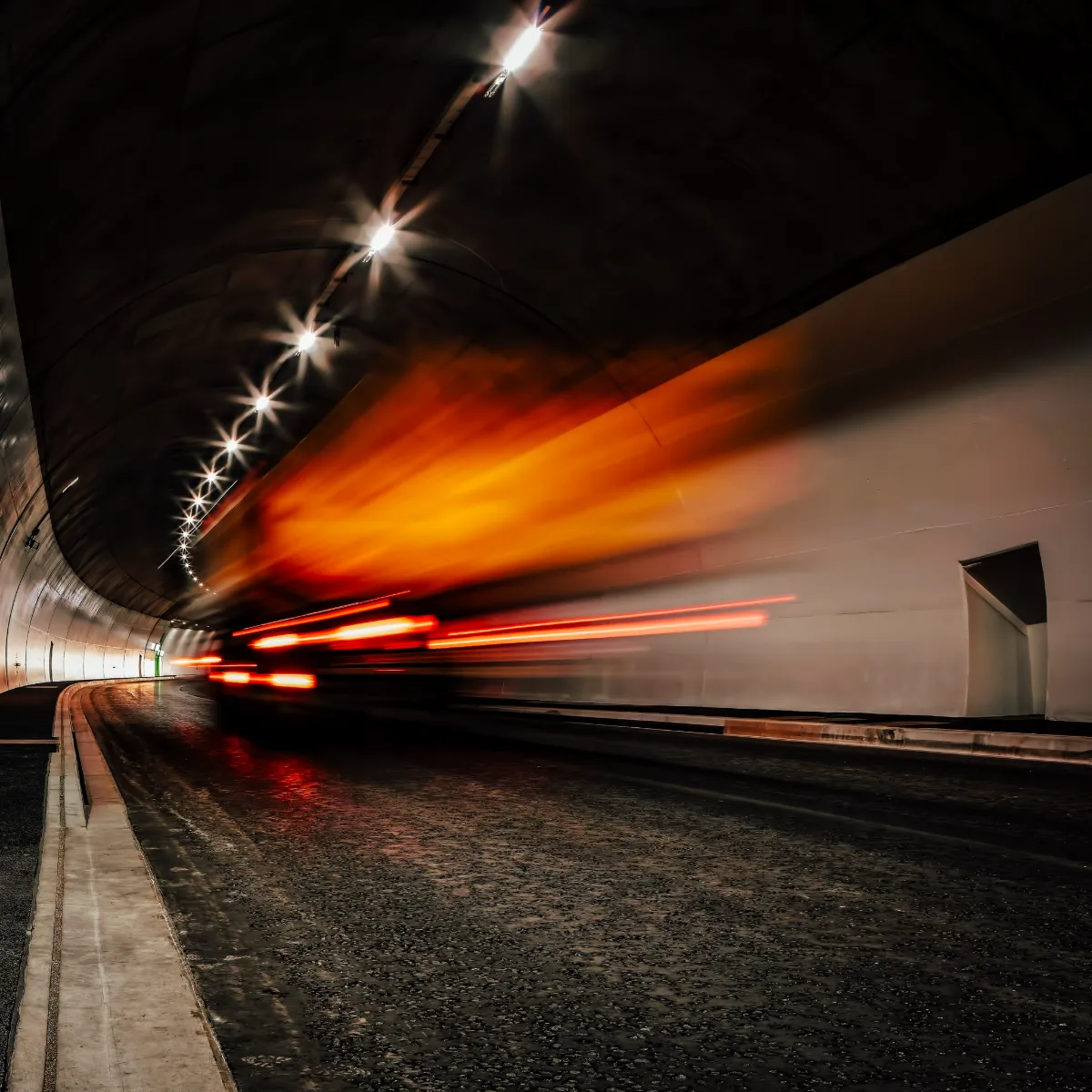 Refrigerated truck moving at speed through a road tunnel, headlights streaking